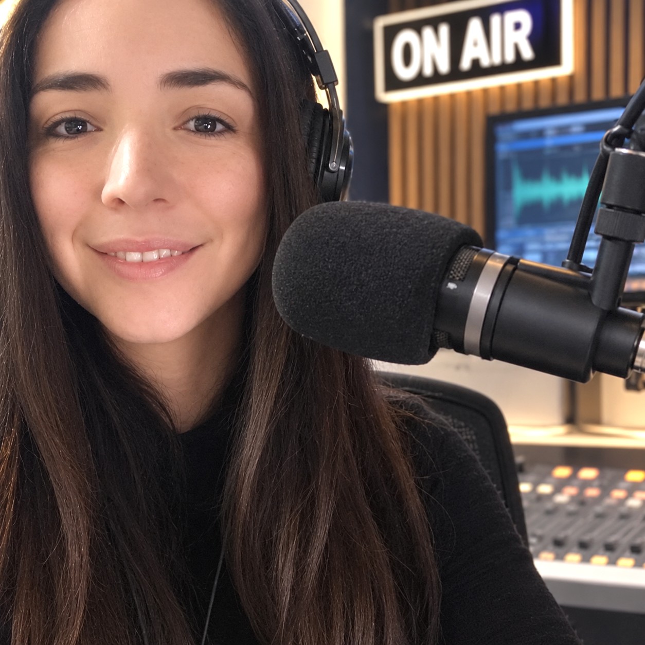 Nelly Jones en la radio, con auriculares y micrófono junto al cartel ON AIR